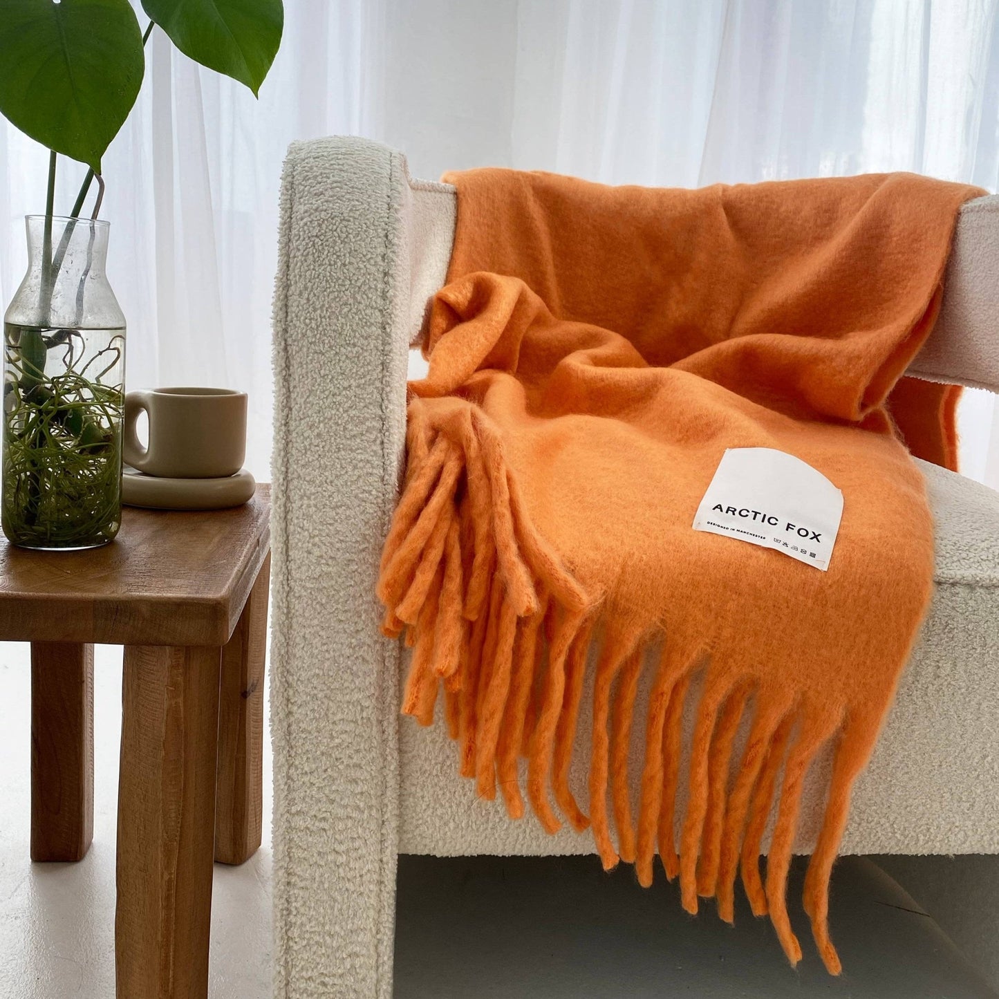 orange blanket with thick tassels thrown over a cream sofa